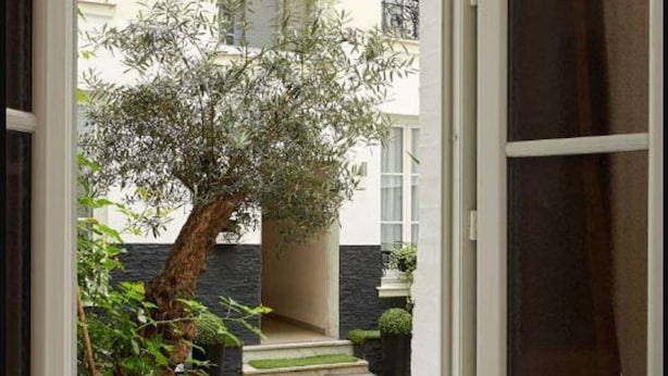 A room with a view of a courtyard, a dining table with food and drinks, and a striped throw on a sofa.
