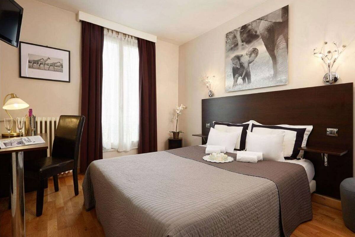 Habitación de hotel con una cama grande, un escritorio con lámpara, una silla, una ventana con cortinas y obras de arte en las paredes.