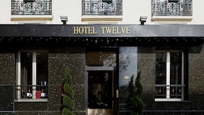 A hotel facade with a classic architectural style, featuring ornate balconies with flower boxes and a prominent "HOTEL TWELVE" sign above the entrance.