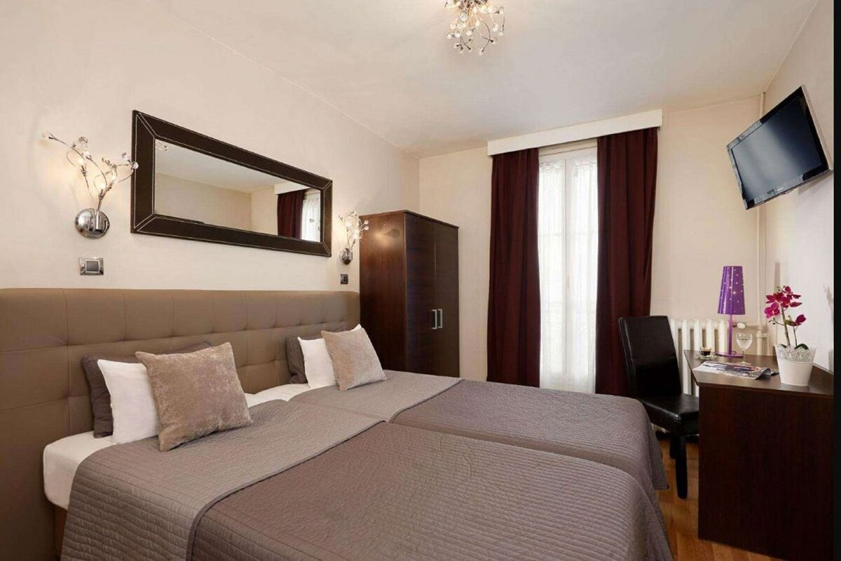 A double bed with a headboard, a desk with a chair, a television, and a window with curtains.