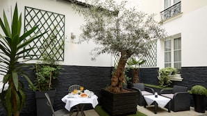 An outdoor patio with a dining table, chairs, and a potted tree.