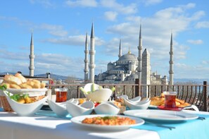 Una mesa con varios platos y vistas de un edificio histórico con múltiples alminares.