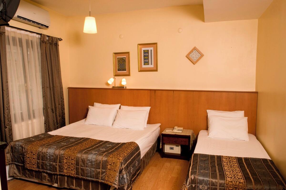 A hotel room with two beds, a wooden headboard, a nightstand with a phone, and a wall-mounted air conditioner.
