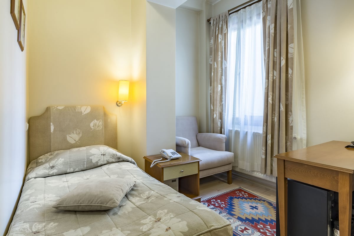 A hotel room with a bed, a chair, a desk, a lamp, and a patterned rug.