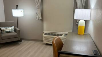 Una habitación de hotel con escritorio, silla, sofá, aire acondicionado y cortinas.