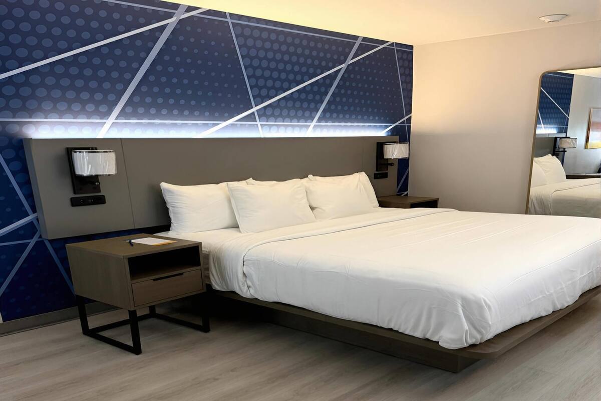 A modern hotel room with a large bed, bedside tables, a mirror, and a geometric-patterned wall.