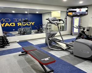 Een sportschool met trainingsapparatuur, een bank en een televisie waarop een menu wordt getoond.