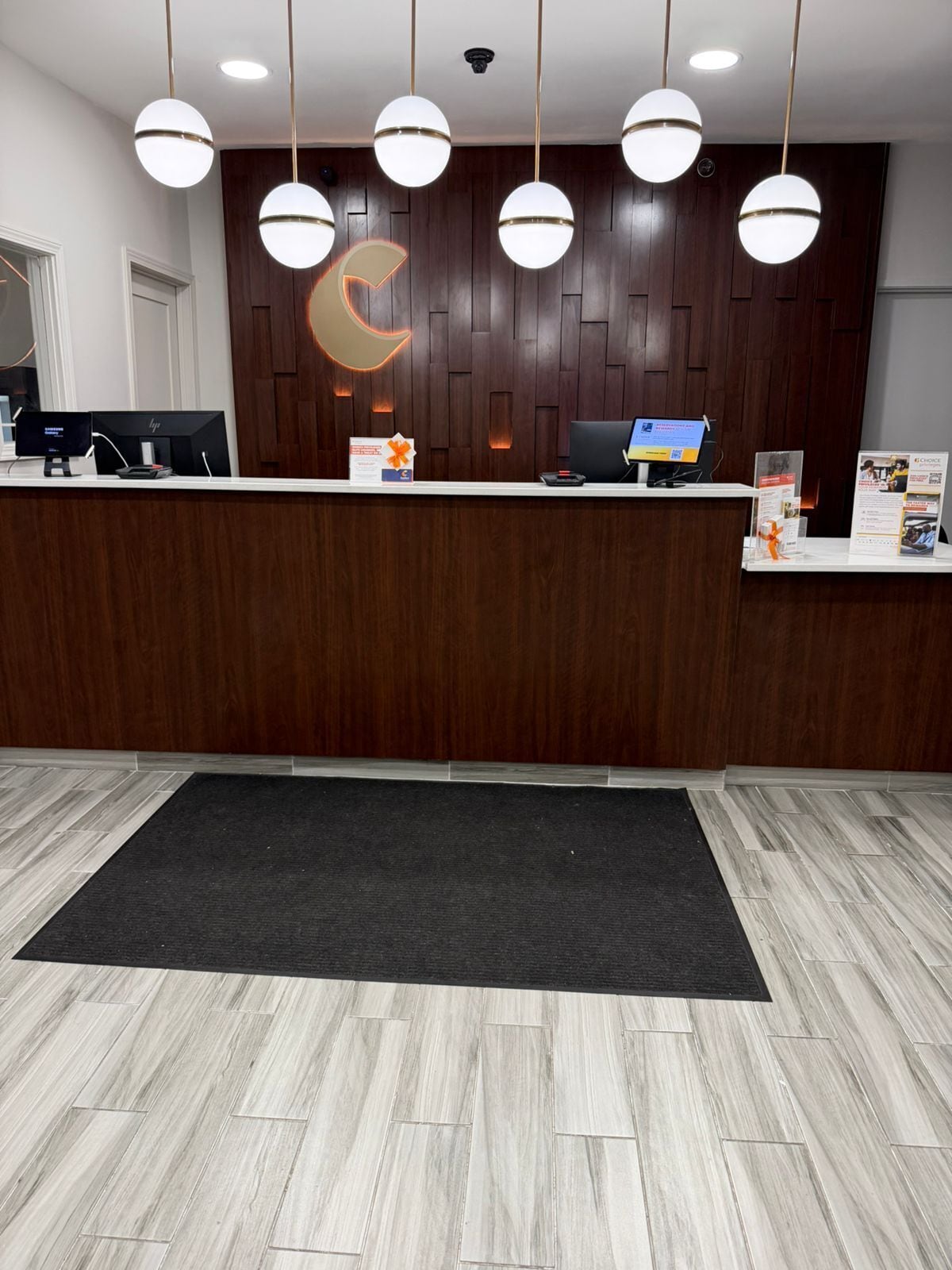 Un comptoir d’accueil avec un logo, un ordinateur, un écran et des brochures.