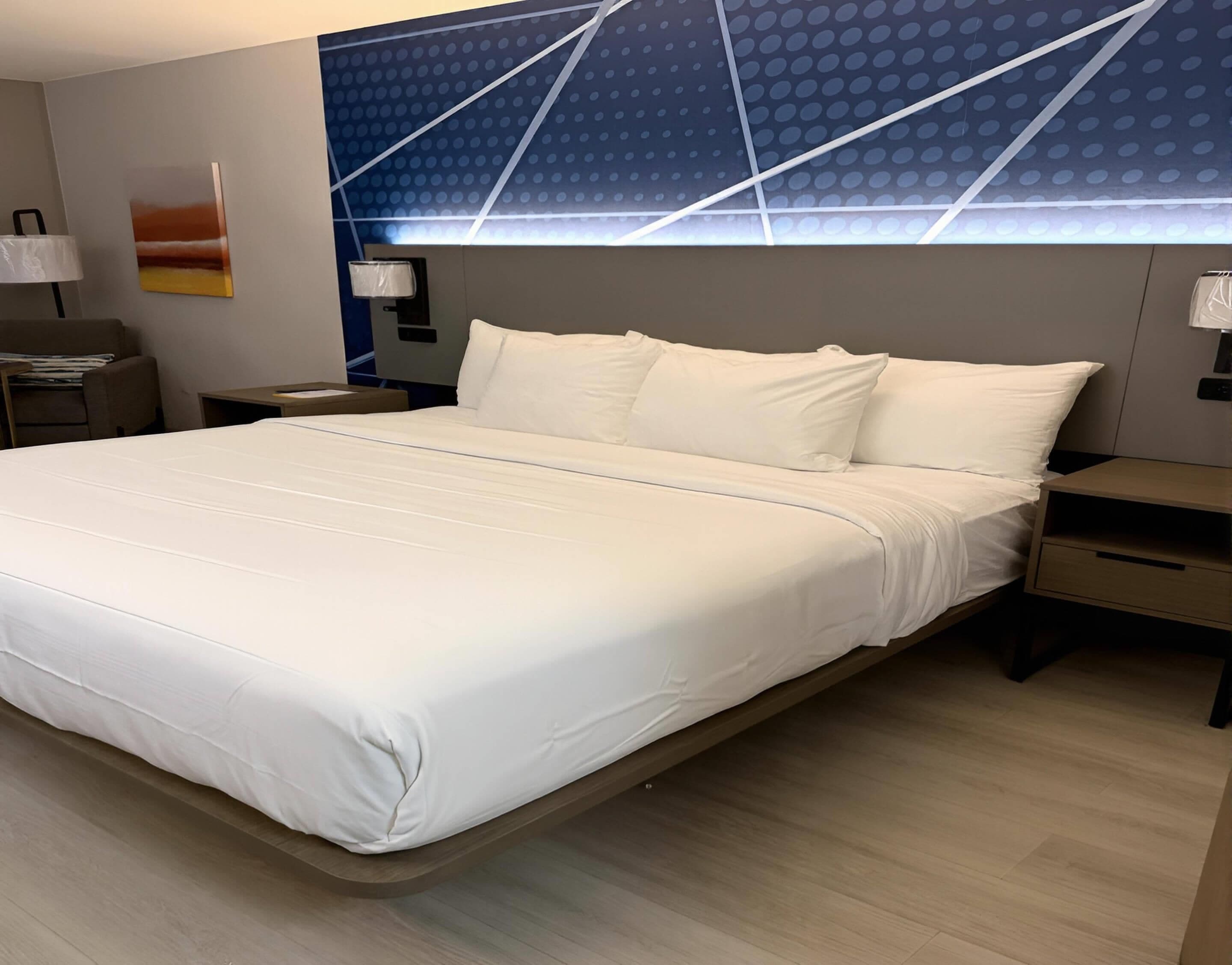 A hotel room with a large bed, two bedside tables, a nightstand, a wall-mounted lamp, and a ceiling with a geometric pattern.