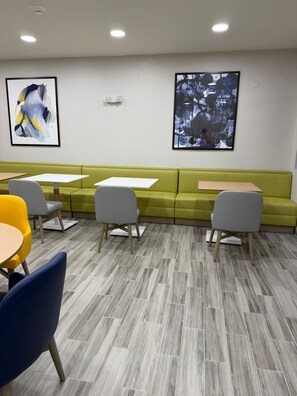 A modern waiting area with a green sofa, white tables, and grey chairs.