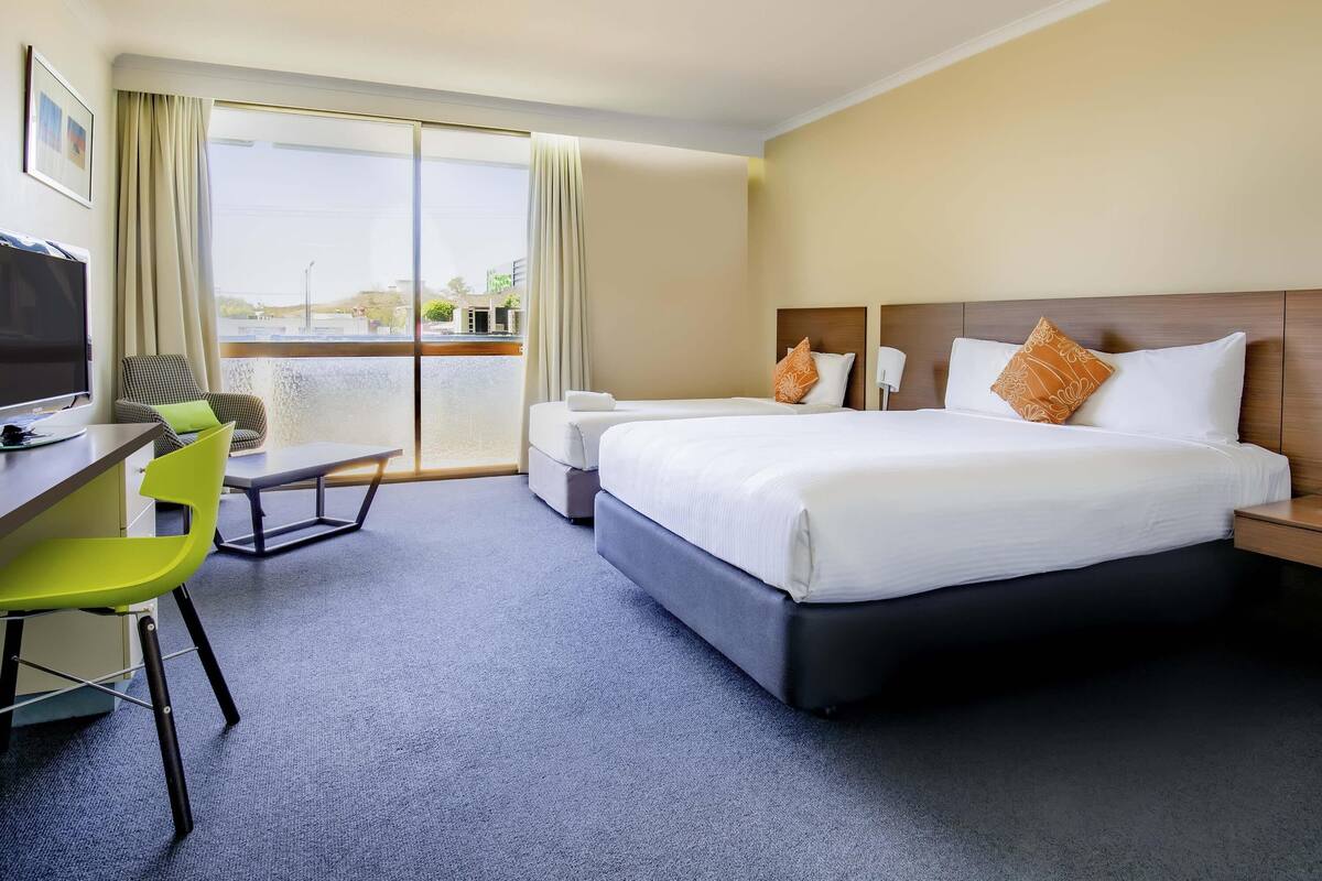 Habitación de hotel con cama, escritorio, silla, televisión y vistas al exterior.