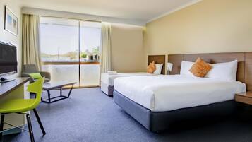 Habitación de hotel con cama, escritorio, silla, televisión y vistas al exterior.
