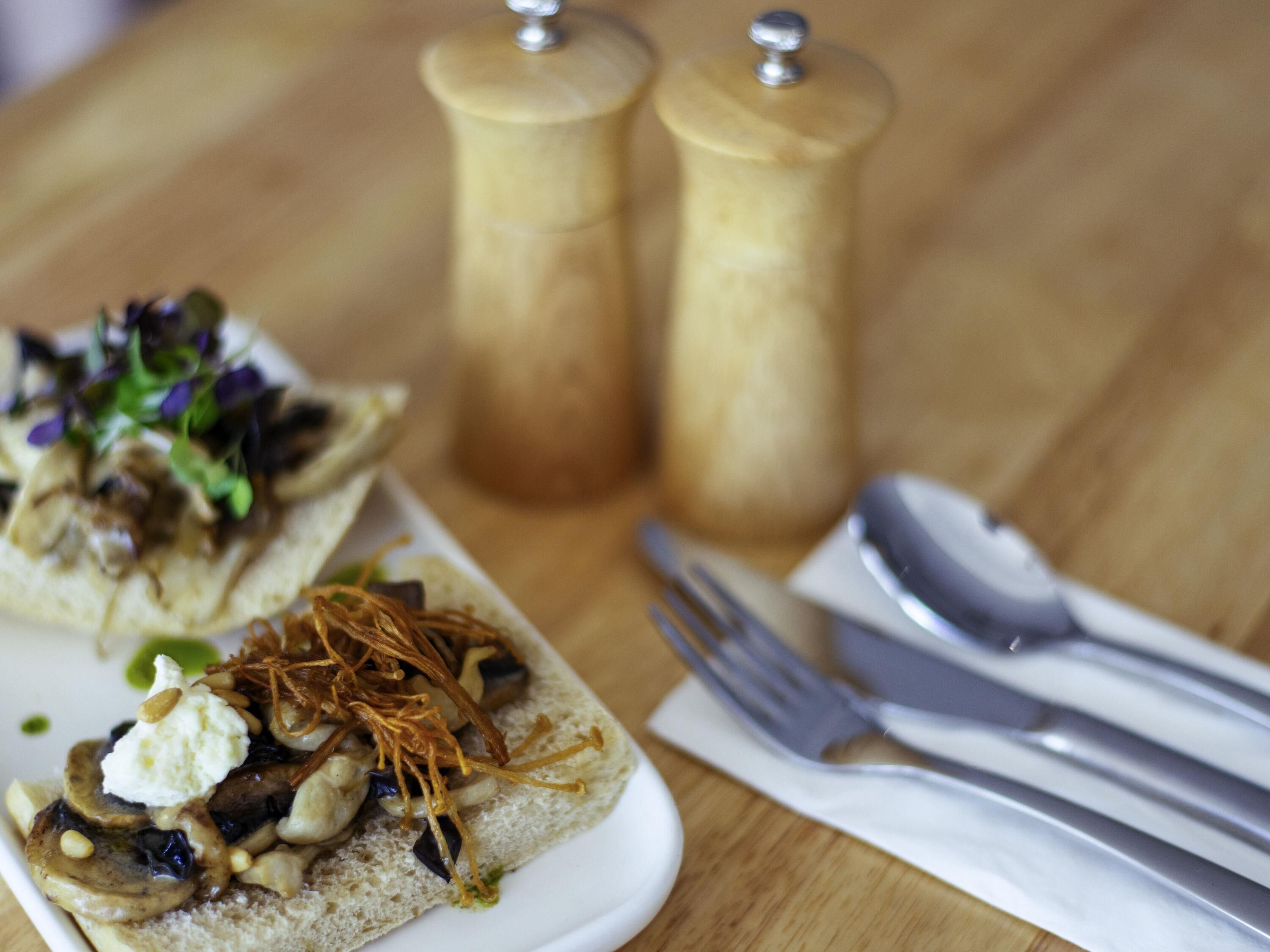 A plate with food items and a set of cutlery on a wooden table.