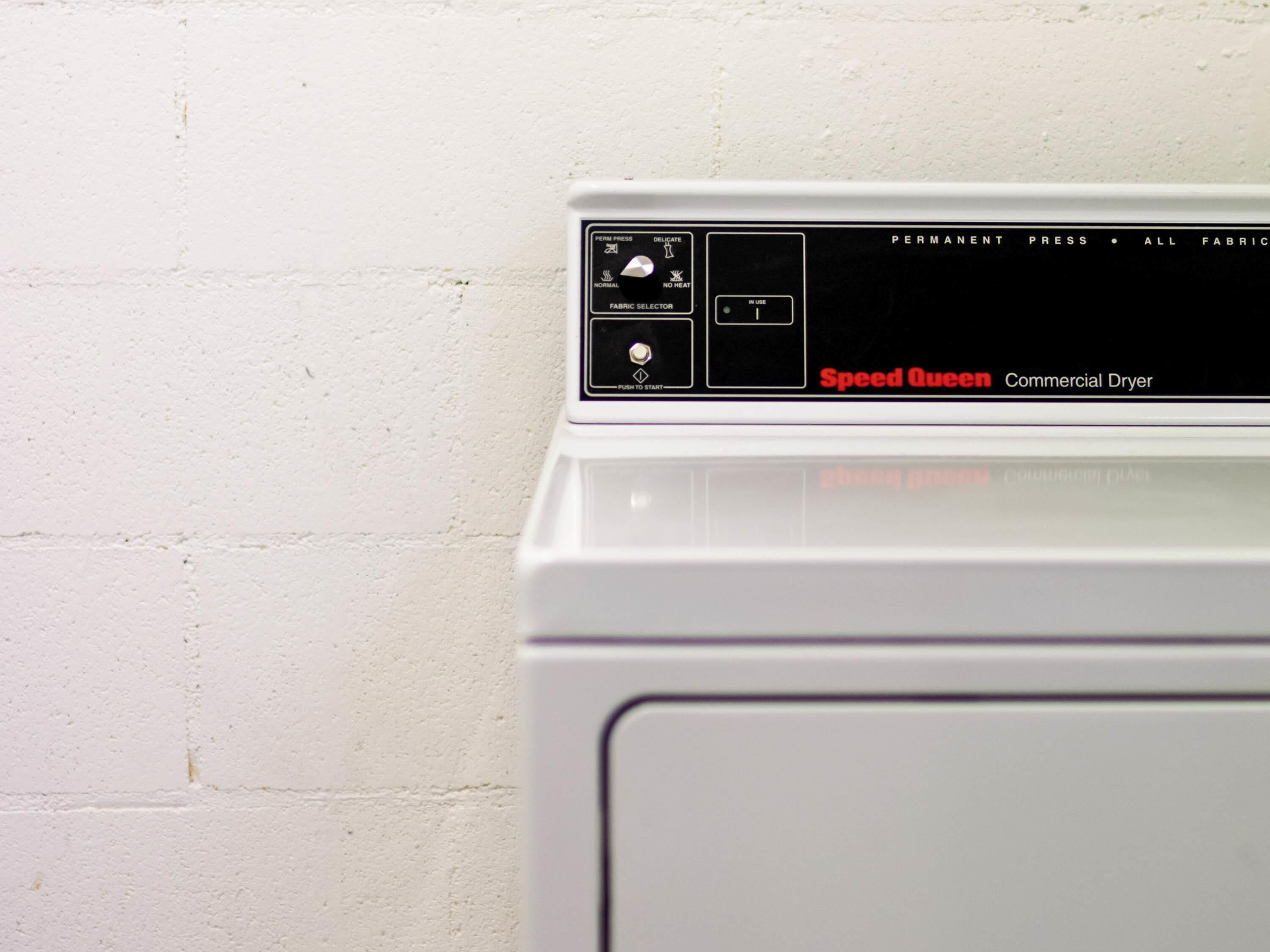 A white commercial dryer with a control panel featuring various settings and a label that reads 'Speed Queen Commercial Dryer.'