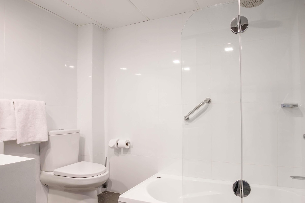 A modern bathroom with a toilet, a glass-enclosed shower, and a bathtub.