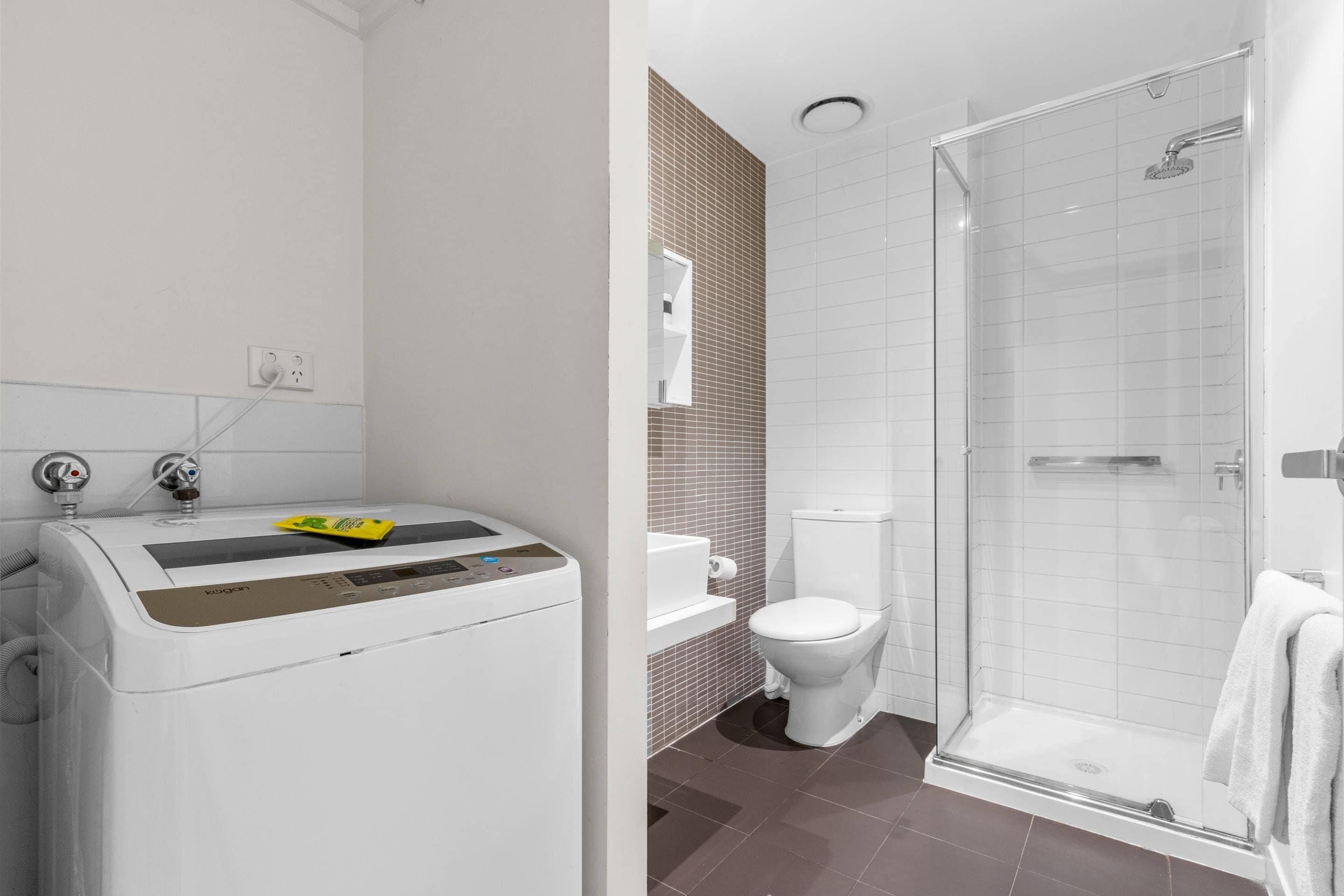 A modern bathroom with a washing machine, toilet, and glass-enclosed shower.