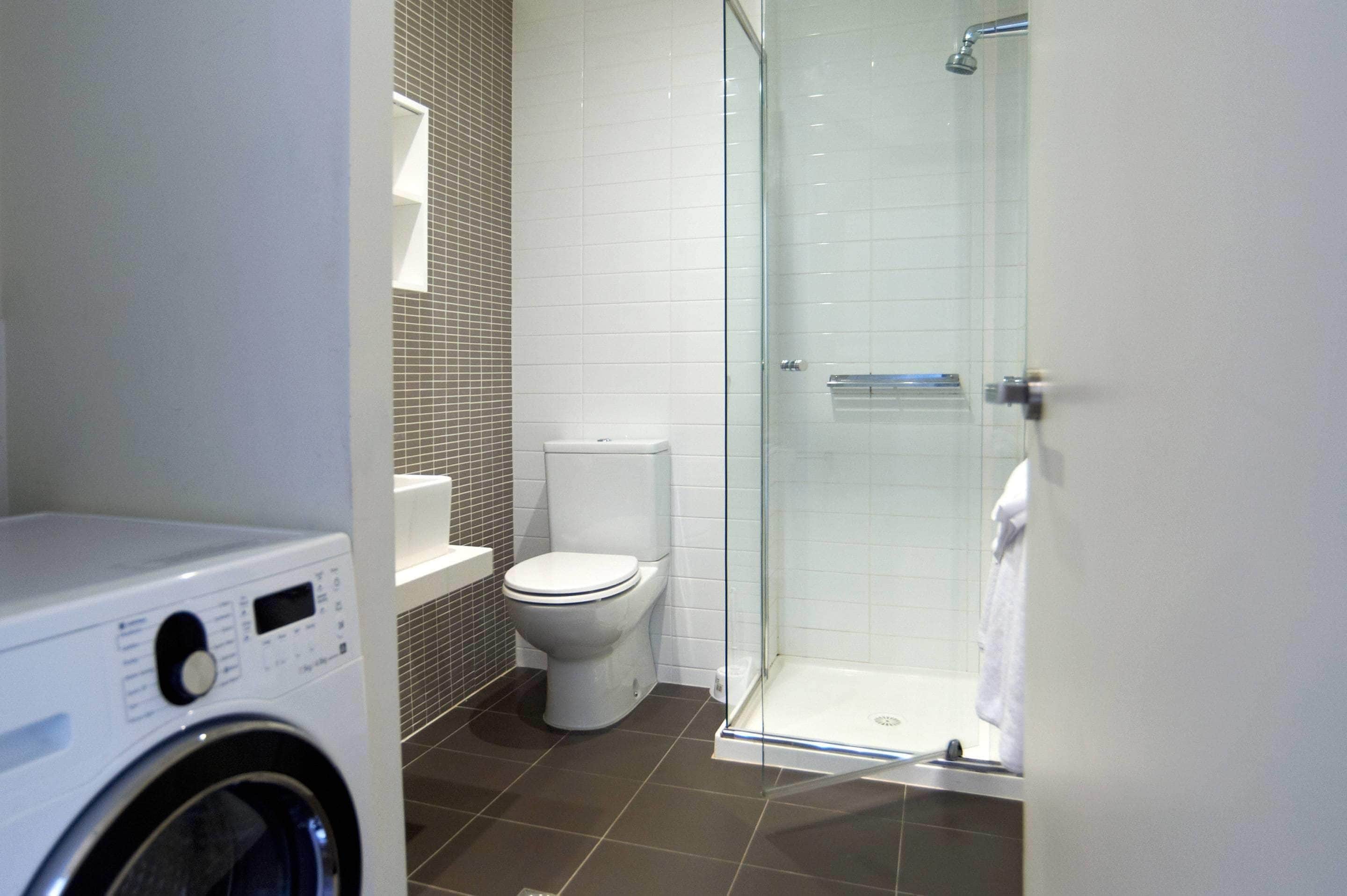 A bathroom with a washing machine, toilet, and glass-enclosed shower.