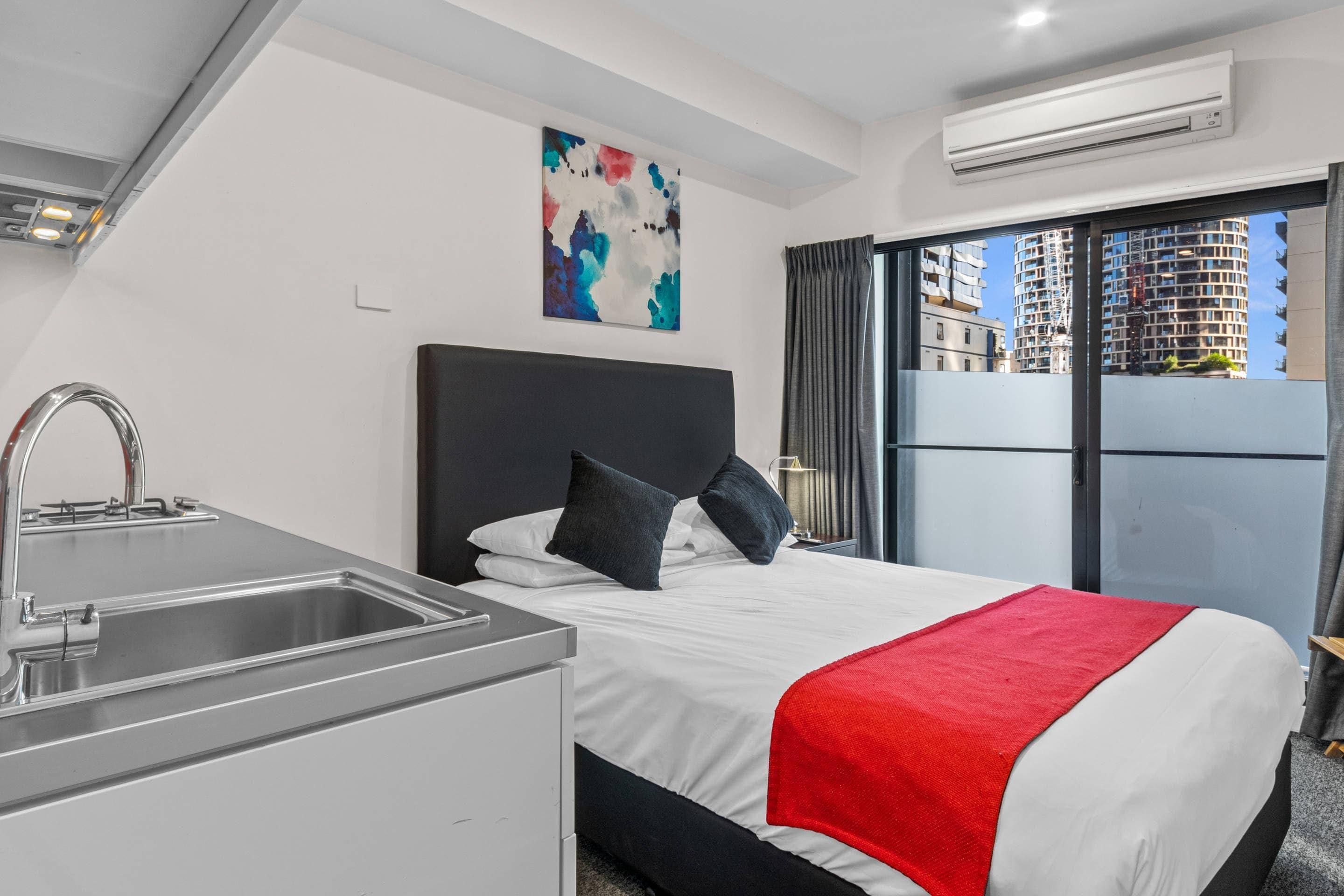 Une chambre d’hôtel avec un lit, un lavabo, un tableau et une vue sur les immeubles.