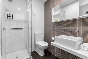 A bathroom with a shower, toilet, sink, and tiled walls. - Comfort Apartments on Elizabeth (Melbourne)