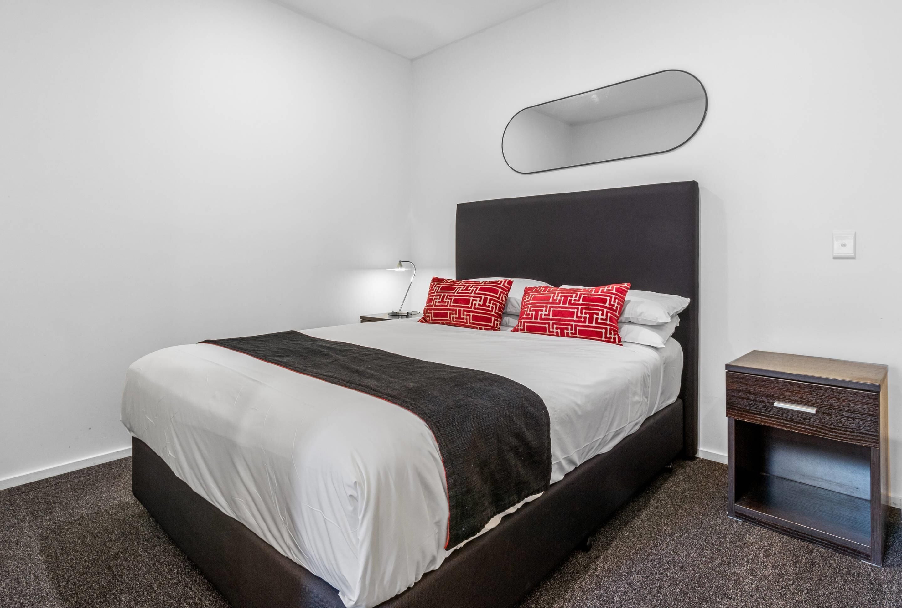 A hotel room with a bed, bedside tables, a wall-mounted mirror, and a carpeted floor.