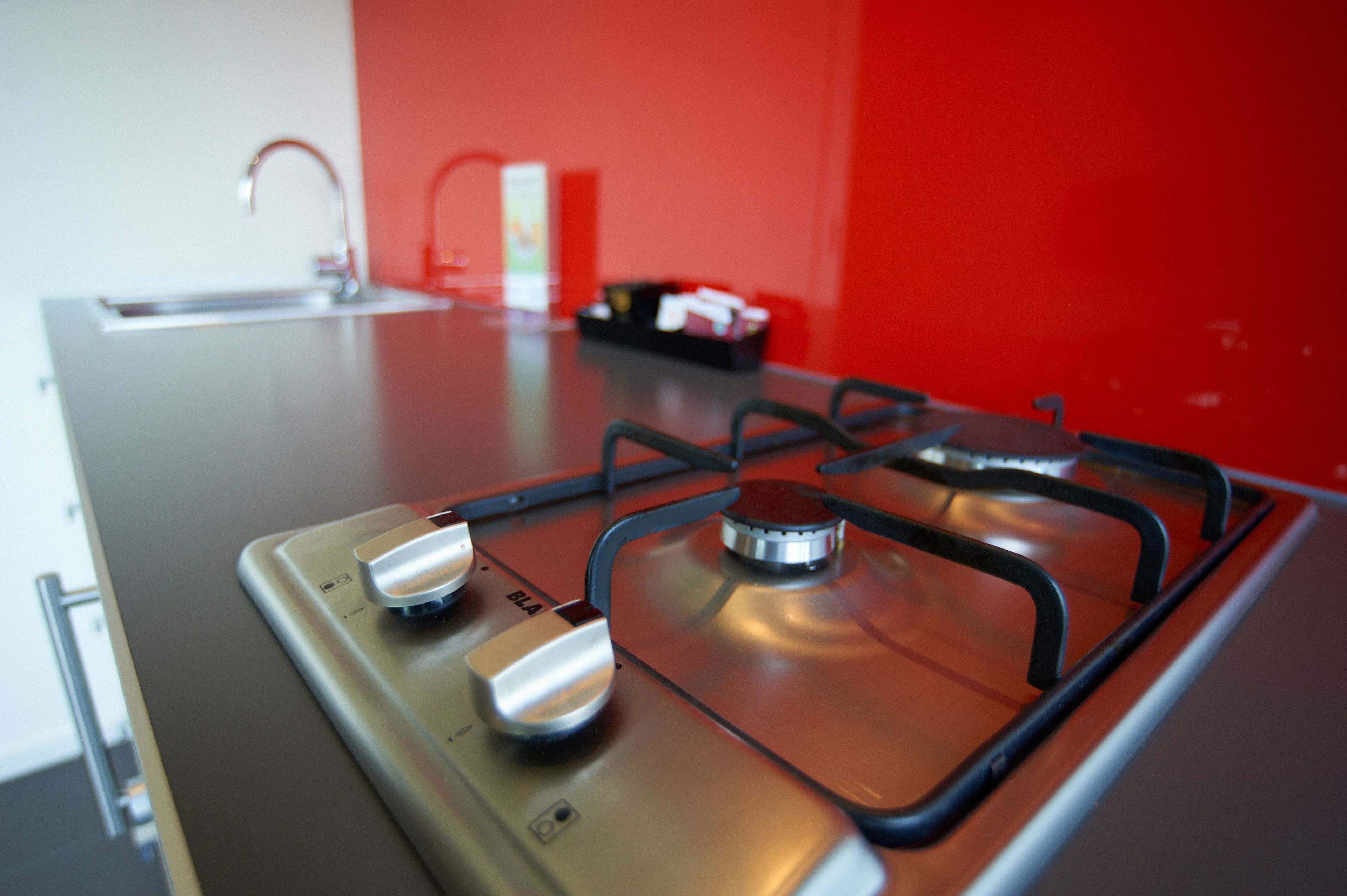 A kitchen with a gas stove, a sink, and a red wall.