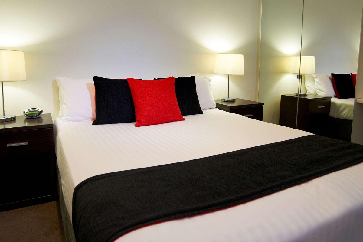 Habitación de hotel con una cama grande, dos mesitas de noche y un espejo en una pared.