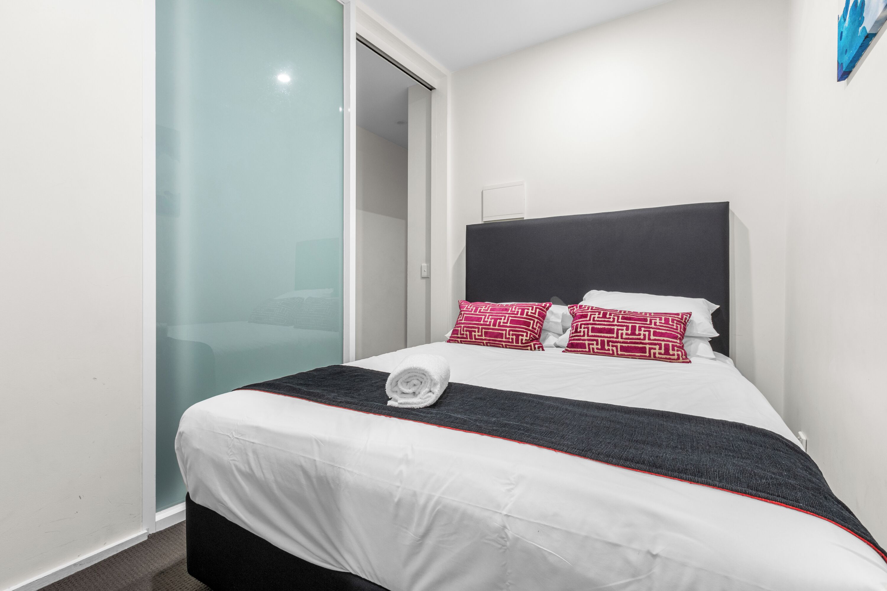 A hotel room with a bed, a glass partition, and a wall-mounted light fixture.