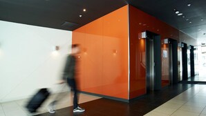 A modern lobby with a bright orange accent wall, a tiled floor, and a person walking with a suitcase. - Comfort Apartments on Elizabeth (Melbourne)