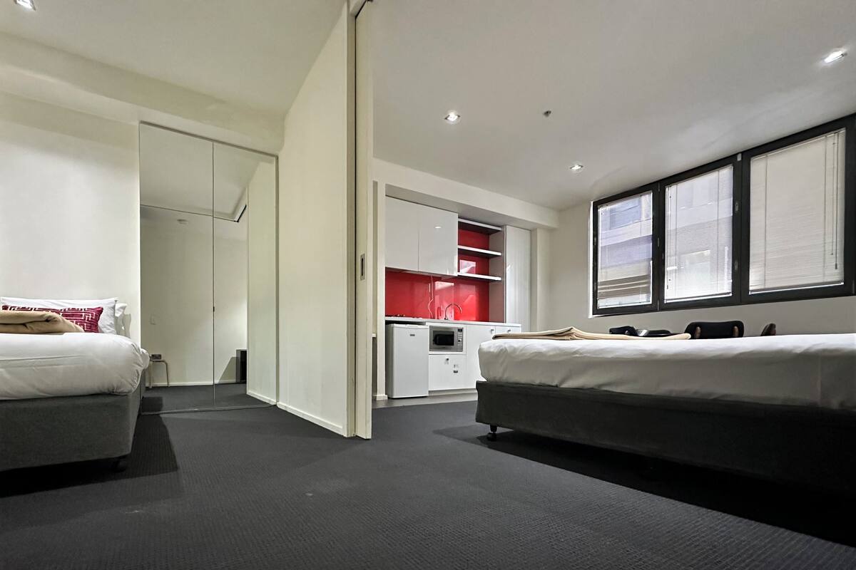 Una habitación de hotel moderna con dos camas, una kitchenette y un armario.