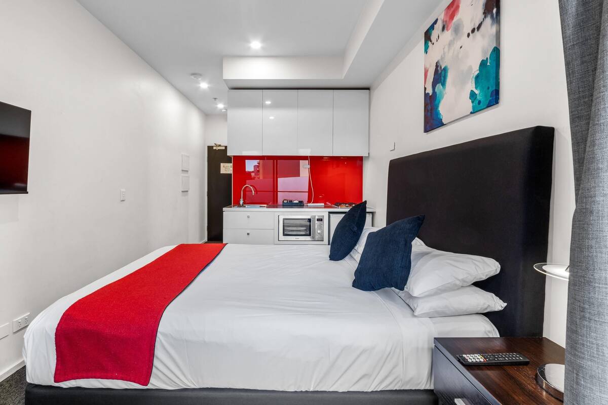 Habitación de hotel moderna con una cama grande, un escritorio y una kitchenette al fondo.
