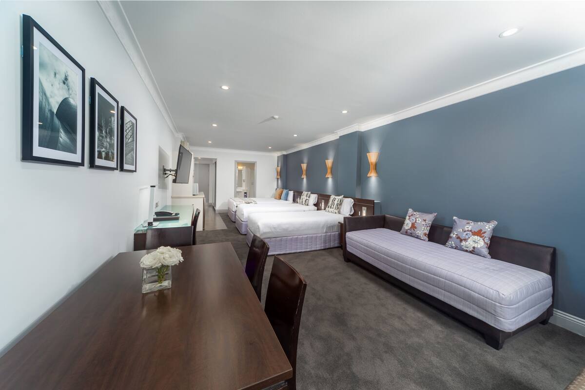 A hotel room with a wooden dining table, two single beds, a sofa, and a small desk with a chair.