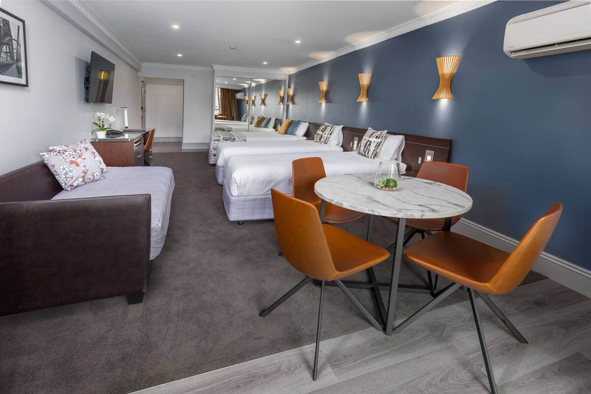 A hotel room with a bed, a sofa, a dining table with chairs, and a desk with a chair.