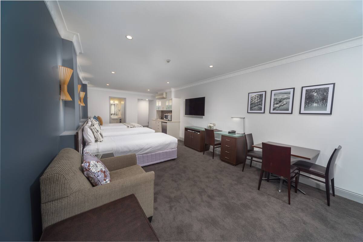 A hotel room with a bed, a desk, a chair, a sofa, and a TV on the wall.