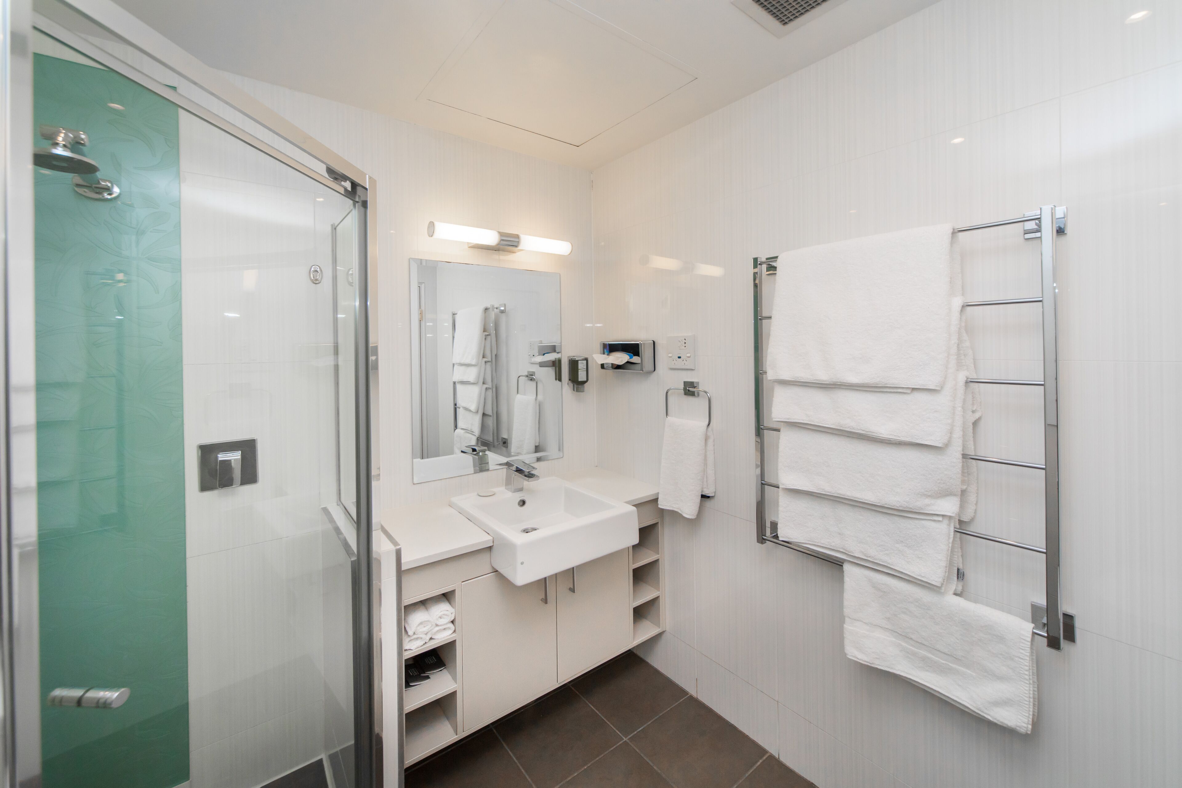 A modern bathroom with a glass shower enclosure, a white sink, and a towel rack.