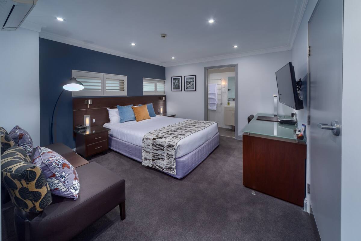 A modern bedroom with a large bed, bedside tables, a desk, and a TV.