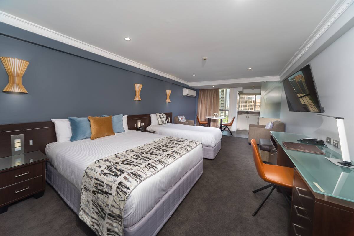 A hotel room with two beds, a desk, a chair, and a TV.