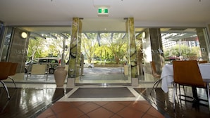 Entrada de hotel con puerta de vidrio, una mesa blanca con mantel blanco y una silla marrón.