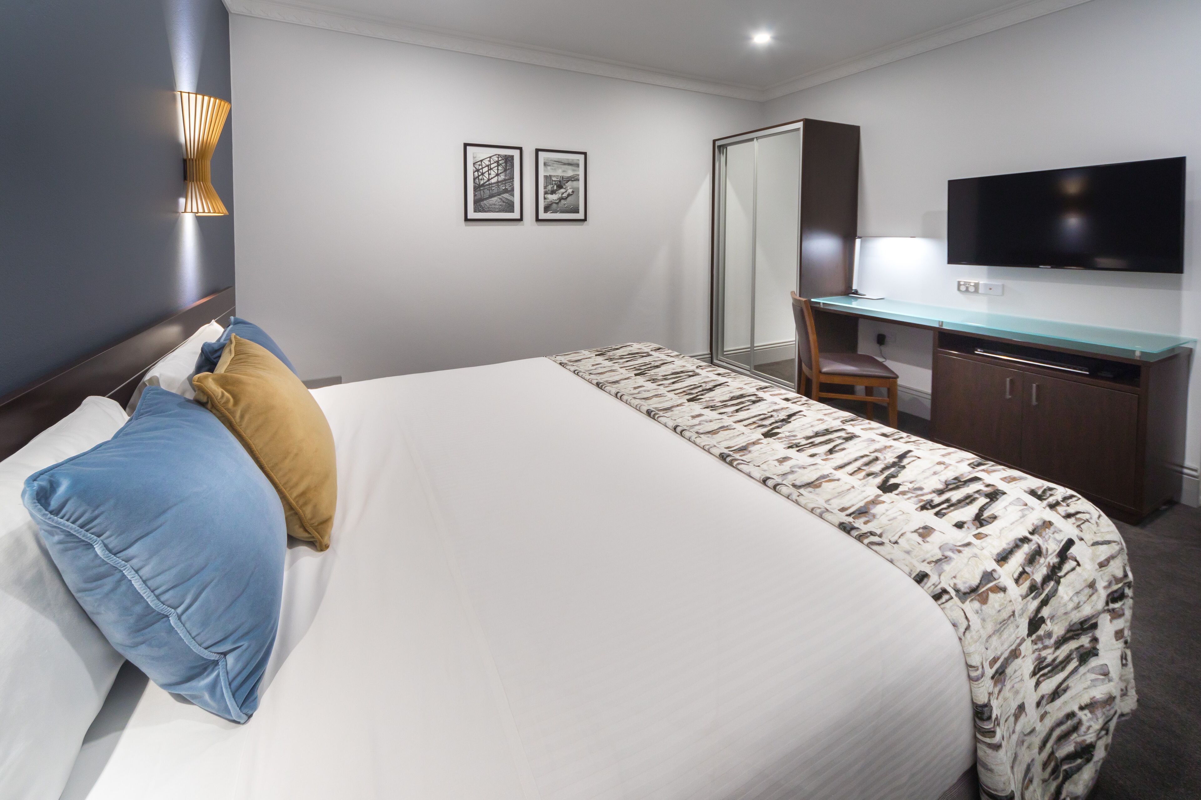 A hotel room with a large bed, a desk with a chair, a flat-screen TV, and two framed pictures on the wall.