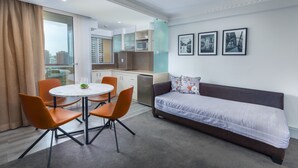 Habitación de hotel moderna con zona de comedor, sofá y cocina al fondo.