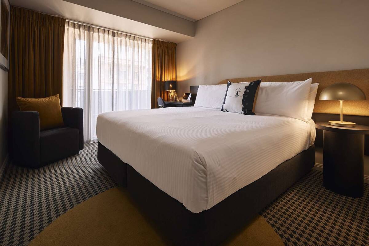 A hotel room with a large bed, a chair, a desk, and a lamp.