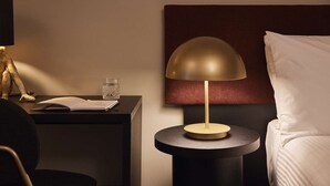 A hotel room with a bedside table, a lamp, a bed, and a nightstand with a book and a glass. - The Capitol Hotel Sydney (Haymarket)