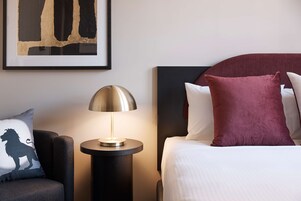 Une chambre d’hôtel bien rangée, avec un lit, une table de chevet dotée d’une lampe et une œuvre d’art encadrée accrochée au mur.