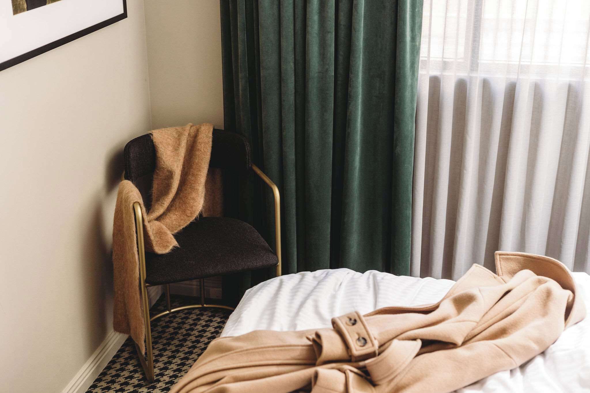 Een kamer met een bed, een stoel met plaid, een raam met gordijnen en een radiator.