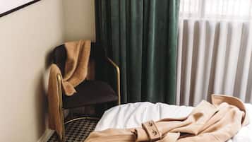 Een kamer met een bed, een stoel met plaid, een raam met gordijnen en een radiator.