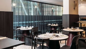 A modern restaurant with round tables and black chairs, featuring a view through a patterned curtain. - The Capitol Hotel Sydney (Haymarket)