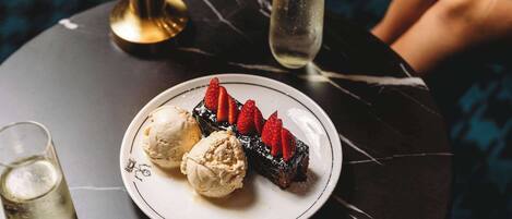 A dessert plate with ice cream and a chocolate dessert topped with strawberries, accompanied by two glasses of a light beverage.