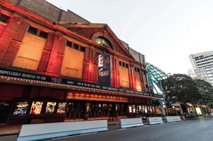 Un théâtre avec une marquise annonçant un spectacle, une grande entrée en verre et une façade en briques.