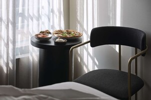 Una habitación con cama, una silla, una mesita con comida y una ventana con cortinas.