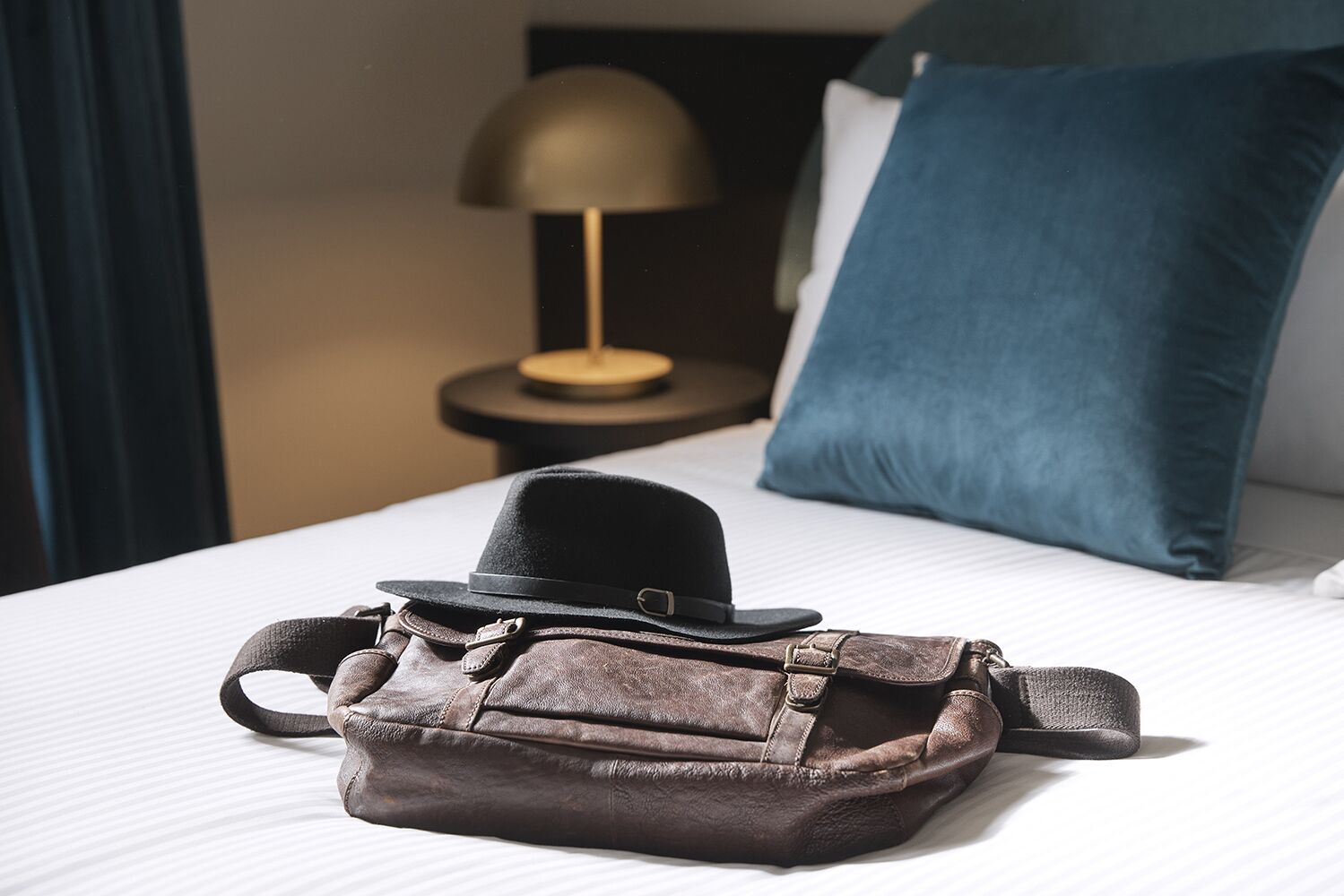 A bed with a black hat and a brown leather bag on it.