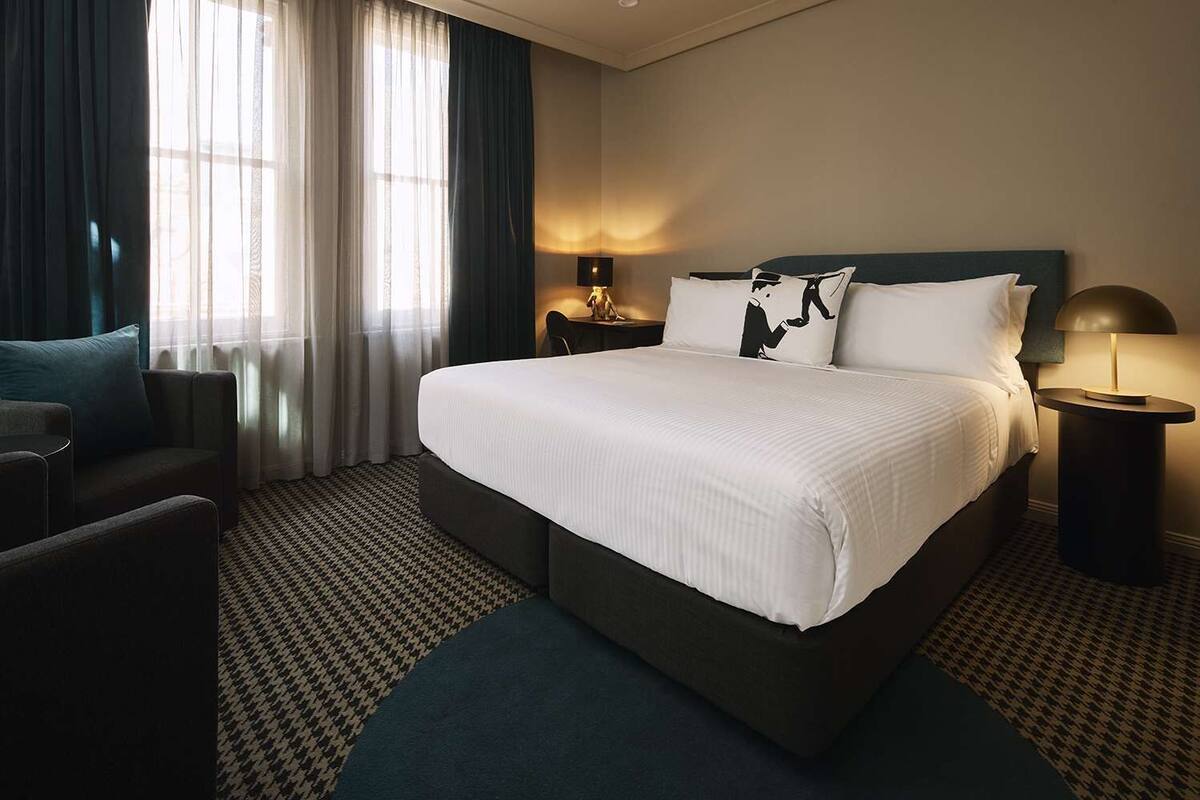 A hotel room with a large bed, a desk, a chair, and a lamp.